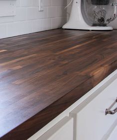 a kitchen counter top with a mixer on the wall in the back ground and white cabinets to the side