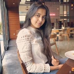 a woman sitting at a table with a plate of food in front of her and looking into the camera