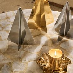 three metal pyramids sitting on top of a marble table next to a lit candle