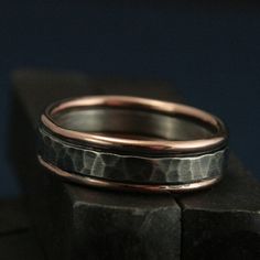 two wedding bands are sitting on top of a black stone block and one has a rose gold band