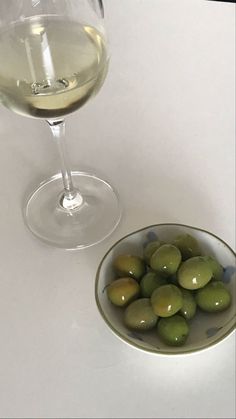 a bowl of olives next to a glass of white wine on a table top