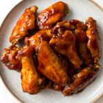 a white plate topped with chicken wings covered in bbq sauce and chopsticks