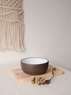 a bowl sitting on top of a wooden cutting board next to a wall hanging with tassels