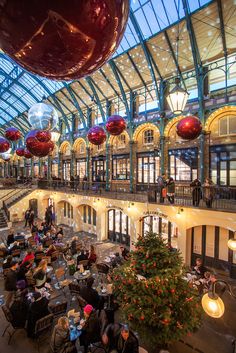 people are sitting at tables in an indoor restaurant with christmas decorations hanging from the ceiling