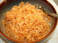 a brown bowl filled with rice on top of a white cloth covered table next to a metal spoon