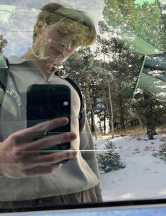 a man is looking at his cell phone while standing in front of a car window