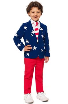 a young boy dressed in an american flag suit and tie, standing with his hands on his hips