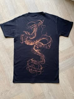 a black t - shirt with an orange dragon on the front and back, sitting on a wooden floor