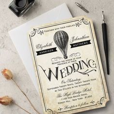 an old fashioned wedding card with a hot air balloon in the sky on it next to some flowers