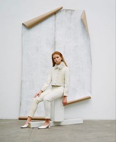 a woman sitting on top of a white chair in front of a large piece of art