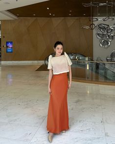 a woman in an orange and white dress is posing for the camera with her hands on her hips