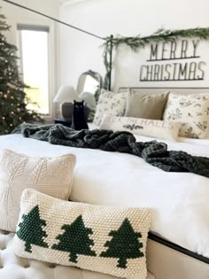 a white bed topped with pillows next to a christmas tree