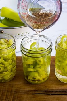 three jars filled with pickles on top of a wooden table