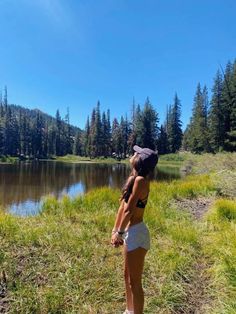 a woman standing on top of a lush green field next to a lake and forest