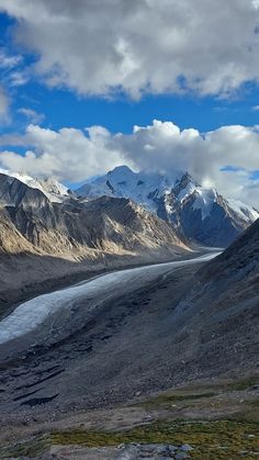 the mountains are covered in snow and ice as clouds hover over them on a sunny day