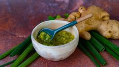 a small white bowl filled with green sauce next to fresh ginger stalks and sliced ginger