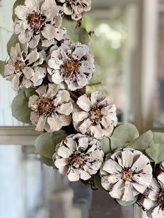 some white flowers and green leaves on a window sill in front of a mirror