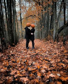 two people with pumpkins on their heads standing in the middle of an autumn forest