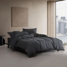 a large bed sitting next to a window in a room with tall buildings behind it