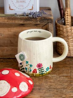 a coffee mug sitting on top of a wooden table next to a red mushroom shaped object