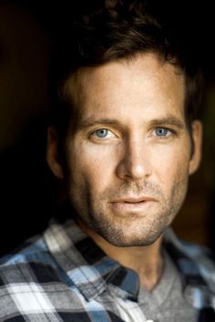 a close up of a person wearing a plaid shirt and looking at the camera with a serious look on his face