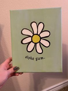 a person holding up a green square with a flower on it that says, alpha gam