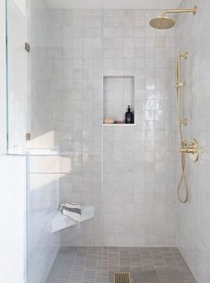 a walk in shower sitting next to a white tiled wall and floor with a gold faucet