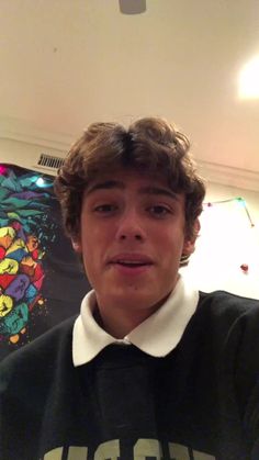 a young man wearing a black and white shirt in front of a wall with graffiti on it