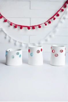 Three white ceramic candle holders with circular cutouts, accented by a garland of red and white pom-poms in the background. Colored Pencil Holder, Crafting Inspiration, Old Candles, Air Dry Clay Projects, Jewelry Holders