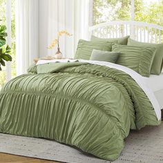 a bed with green comforter and pillows in a room next to a window,