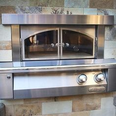 two ovens are built into the side of a stone wall with metal trim around them