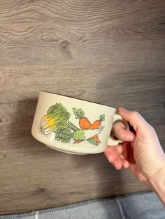 a person holding a coffee cup in front of a wooden wall with an image of carrots and broccoli on it