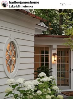 a house with white flowers in front of it and an open window on the side