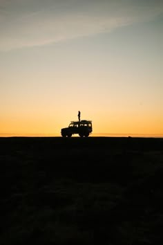 a person standing on top of a vehicle in the middle of a field at sunset