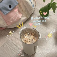 a cup of coffee sitting on top of a wooden floor next to a backpack and flowers