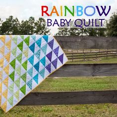 a rainbow baby quilt sitting on top of a wooden fence next to a green field