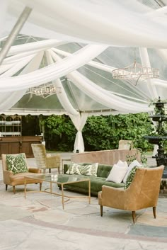 an outdoor living area with couches, chairs and tables under a white drape