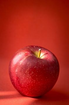 an apple sitting on top of a red surface next to a shadow from the sun