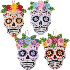 three sugar skulls decorated with flowers and leaves are hanging from the side of a white wall