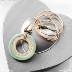 two necklaces are sitting on top of a metal plate and one has a circular pendant with