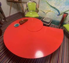 a red table sitting on top of a colorful rug next to two green chairs and a painting