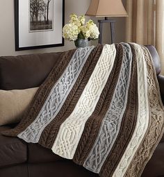 a couch with a blanket on top of it next to a lamp and flowers in a vase