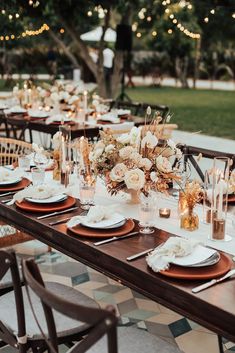 an outdoor dinner table set up with candles, plates and place settings for the guests