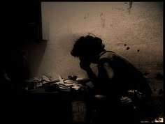 black and white photograph of a person sitting in a room with food on the floor