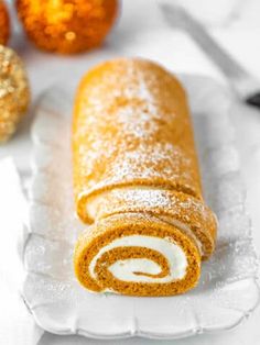 a pumpkin roll on a white plate with orange decorations in the background and text overlay that reads, pumpkin roll