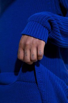 a person with their hand on the pocket of a blue sweater