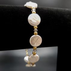 An elegant freshwater coin pearl clasp bracelet is ready to wear to a dressier event or be the perfect gift for someone lovely in your life. The bracelet includes flat, round 12 mm white pearl beads, clear bicone high-quality sparkly clear crystals, and delicate matte gold-colored glass spacer beads. The bracelet's clasp is a 14K gold-filled lobster clasp. The bracelet's stringing material is a high-quality, flexible gold-colored stringing wire. For added security, wire guards are placed on each Elegant Gold Stretch Bracelet, Formal Round Pearl Bracelet, Adjustable Pearl Bracelet, White Jubilee Crystal Bracelet For Anniversary, White Pearl Bangle Jewelry, Elegant Yellow Gold Stretch Bracelet, Elegant Hypoallergenic Name Bracelet With Round Beads, Adjustable Round Pearl Bracelet For Formal Occasions, Round Pearl Beaded Bracelets For Wedding