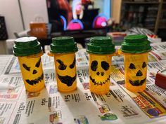 three plastic cups with faces painted on them sitting on top of a news paper covered table