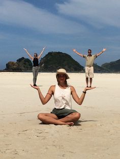 three people doing yoga on the beach with their hands in the air