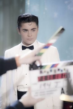 a man in a tuxedo holding a movie clapper and pointing to it